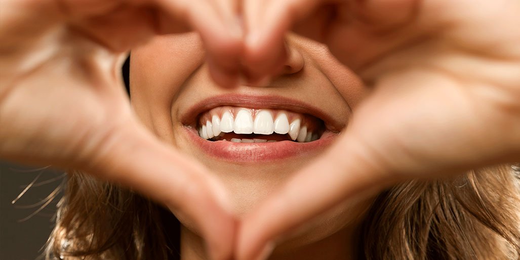 Ragazza sorridente che forma un cuore con le mani, in primo piano.
